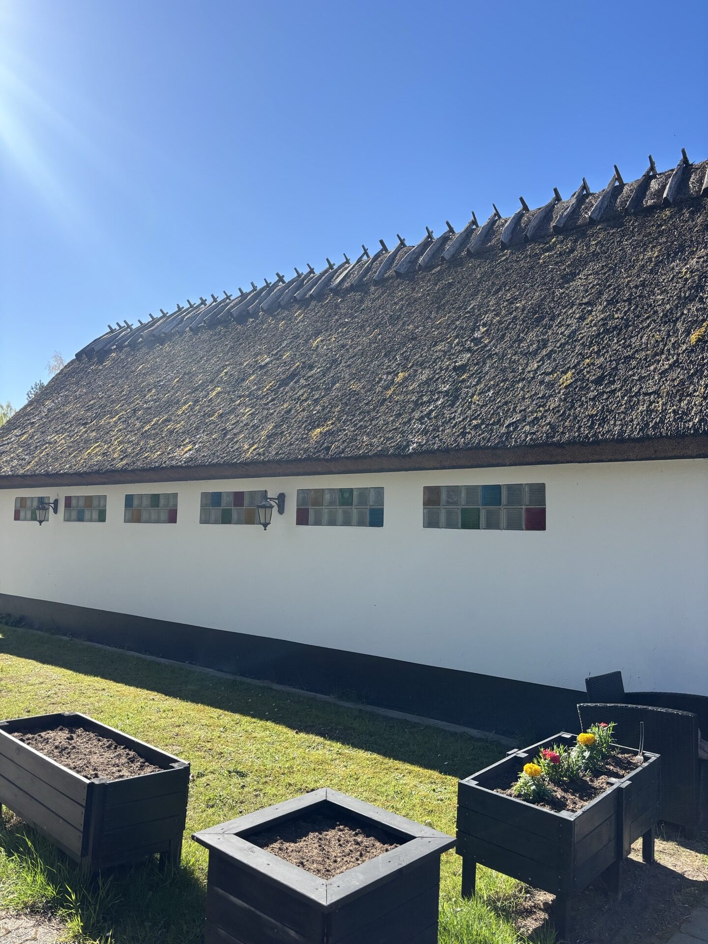 Stråtagshusets lange facade med haverabatter og plantekasser